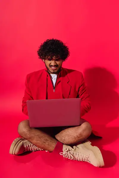 A young Indian man in vibrant attire sitting on the floor, engrossed in his laptop. — Stock Photo