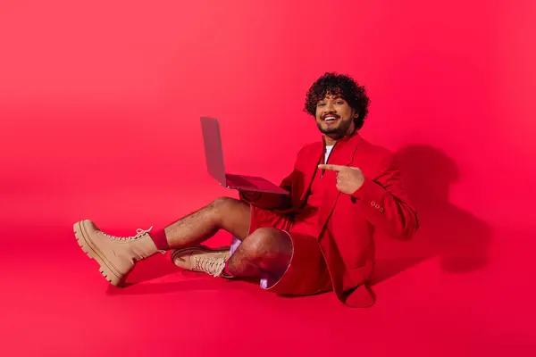 Young Indian man in vibrant outfit sits on floor, engrossed in laptop work. — Stock Photo
