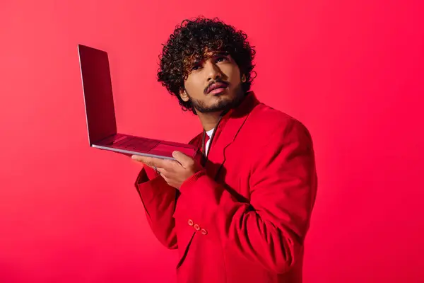 Bonito jovem indiano em um vibrante terno vermelho segura com confiança um laptop. — Fotografia de Stock
