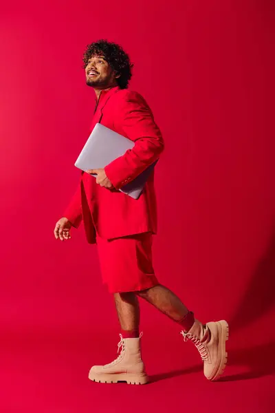 Um jovem indiano elegante em um terno vermelho impressionante segurando um laptop. — Fotografia de Stock