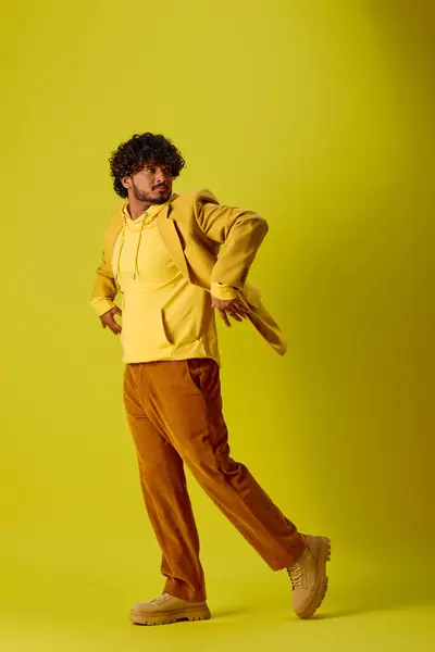 Schöner indischer Mann in gelbem Hemd und brauner Hose posiert vor buntem Hintergrund. — Stockfoto