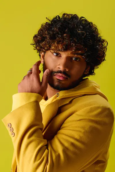 Handsome Indian man with curly hair striking a pose in a yellow jacket on a vivid backdrop. — Stock Photo