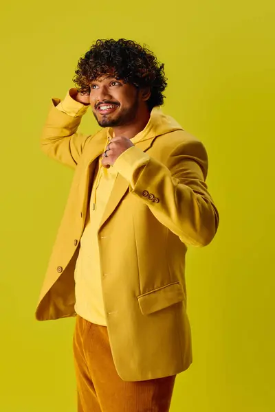 Bonito homem indiano em casaco amarelo e calças castanhas posando em fundo vívido. — Fotografia de Stock