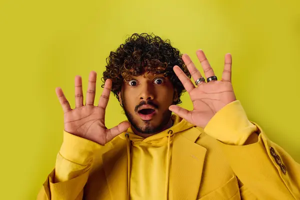 Handsome Indian man in vibrant yellow jacket having fun posing with hands on face. — Stock Photo