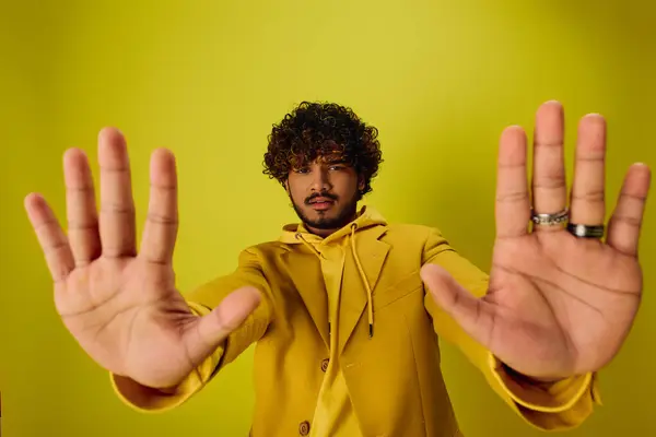 Ein hübscher junger indischer Mann in einem gelben Kapuzenpullover hält seine Hände in die Höhe. — Stockfoto