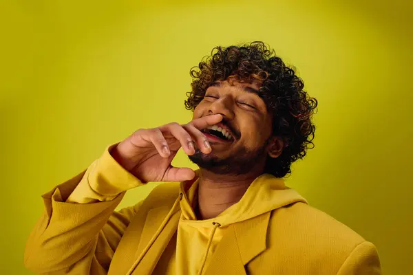 A handsome, young Indian man in a yellow hoodie against a vivid backdrop. — Stock Photo