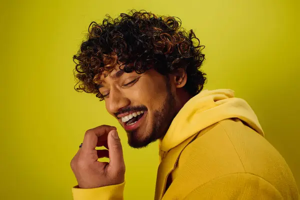 A handsome young Indian man with curly hair striking a pose in a vibrant yellow jacket on a vivid backdrop. — Stock Photo