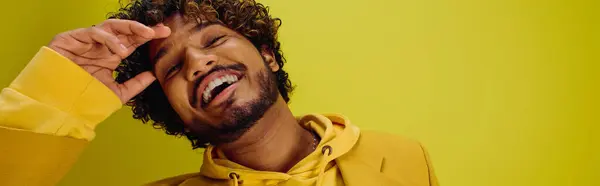 Ein gutaussehender junger indischer Mann in einem leuchtend gelben Kapuzenpulli macht vor einer eindrucksvollen Kulisse einen lustigen Gesichtsausdruck. — Stockfoto