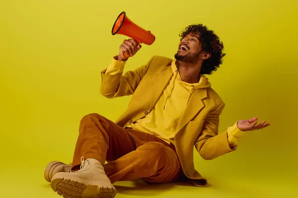 Man in vibrant attire sits holding red and orange megaphone. — Stock Photo