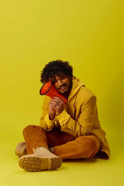 Bonito homem indiano em roupa colorida senta-se segurando megafone vermelho. — Fotografia de Stock