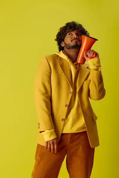 Handsome Indian man in yellow jacket holding red megaphone against vivid backdrop. — Stock Photo