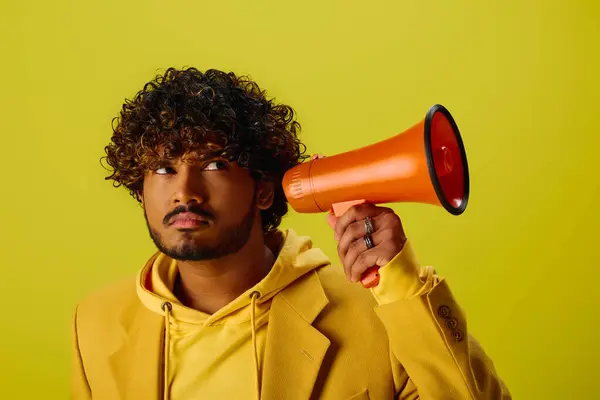 Um belo jovem indiano com um capuz amarelo segurando um megafone vermelho. — Fotografia de Stock