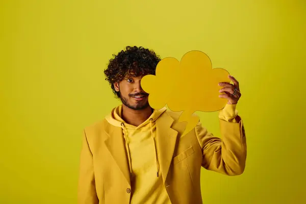 Bonito homem indiano em casaco amarelo segurando bolha de discurso contra fundo vibrante. — Fotografia de Stock