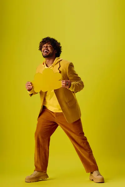 Handsome young Indian man in a vibrant suit confidently holds a dazzling yellow speech bubble. — Stock Photo