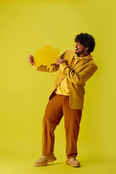 Jeune homme indien en veste jaune tient une bulle de discours jaune sur fond vibrant. — Photo de stock