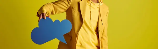 Handsome young Indian man in yellow raincoat holding a blue speech bubble against a vivid backdrop. — Stock Photo