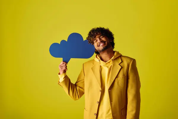 Handsome young Indian man in yellow suit holding blue speech bubble on vivid backdrop. — Stock Photo