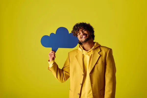 Bonito jovem indiano em terno amarelo segurando bolha de fala azul em fundo vívido. — Fotografia de Stock