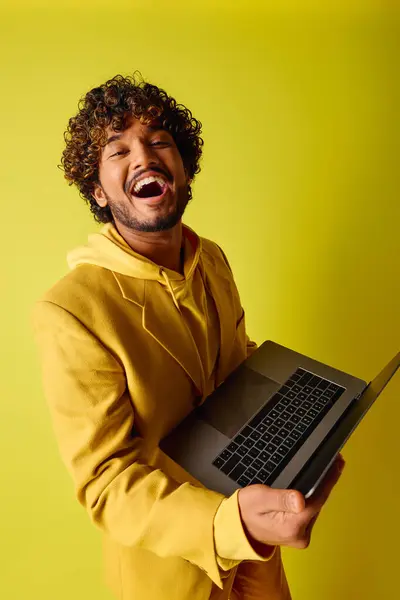 A handsome young Indian man in a vibrant outfit holding a laptop with his mouth open. — Stock Photo