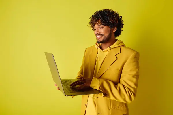 A handsome young Indian man in a vibrant yellow suit holds a laptop. — Stock Photo
