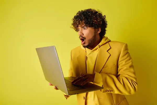 A stylish young Indian man in a yellow suit confidently holding a laptop. — Stock Photo