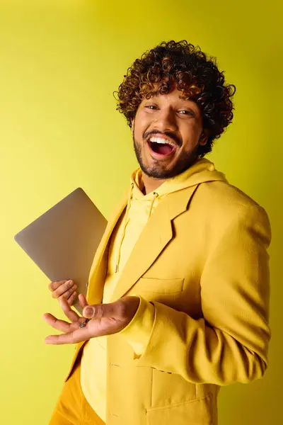 Handsome Indian man in a vibrant yellow suit confidently holds a laptop. — Stock Photo