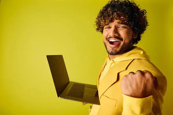 Handsome young Indian man in a vibrant yellow suit confidently holds a laptop. — Stock Photo