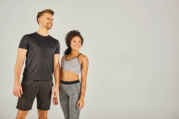 A man and a woman, both in active wear, standing side by side against a grey background in a studio setting. — Stock Photo