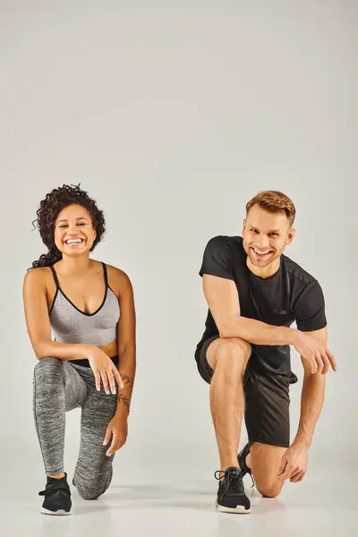 Young interracial sport couple squatting together in active wear on grey background in a studio setting. — Stock Photo