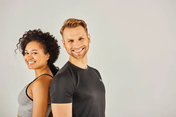 Young interracial sport couple in active wear strike a dynamic pose together against a grey studio backdrop. — Stock Photo