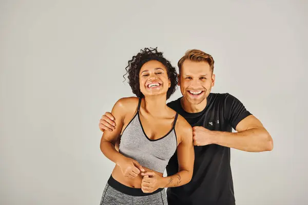 Un jeune couple sportif interracial en tenue active posant en toute confiance pour la caméra dans un studio sur fond gris. — Photo de stock