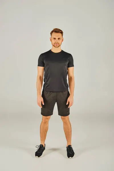Um jovem em uma camiseta preta e shorts posa confiantemente na frente de um fundo branco. — Fotografia de Stock