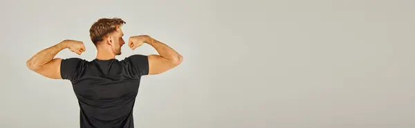 A young athletic man in active wear flexing his muscles in front of a gray background in a studio. — Stock Photo