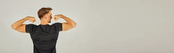 A young athletic man in active wear flexing his muscles in front of a gray background in a studio. — Stock Photo