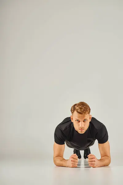 Un giovane atletico in abbigliamento attivo, che esegue flessioni su uno sfondo grigio in uno studio. — Foto stock