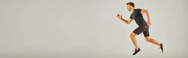 Um jovem atlético em uso ativo correndo energeticamente em um fundo cinza em um estúdio. — Fotografia de Stock