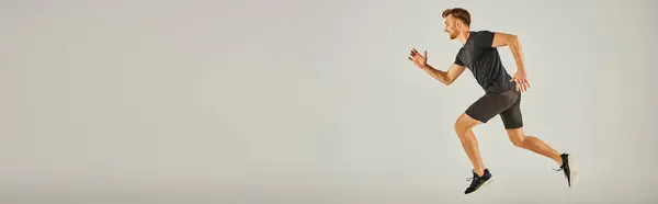 A young athletic man in active wear running energetically on a gray background in a studio setting. — Stock Photo