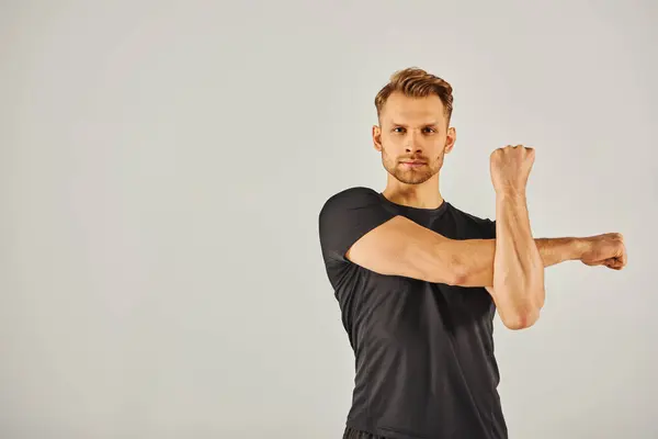 Un jeune homme sportif en tenue active fléchit son bras sur un fond gris dans un affichage dynamique de force et de remise en forme. — Photo de stock