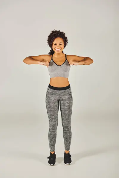 Jovem, apto mulher afro-americana marcando uma pose graciosa com os braços estendidos em desgaste ativo no fundo do estúdio cinza. — Stock Photo