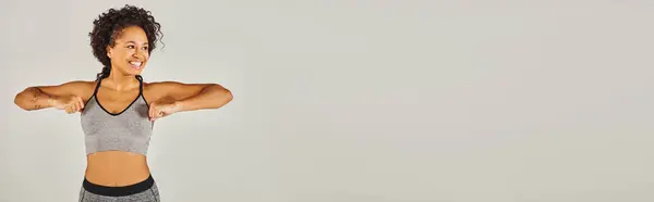 A young fit African American woman in active wear flexes her arms confidently in front of a white background. — Stock Photo
