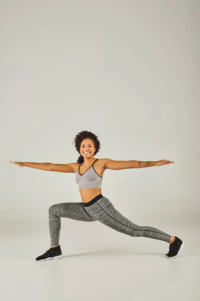 A young African American woman dressed in activewear gracefully performs a yoga pose on a white background. — Stock Photo