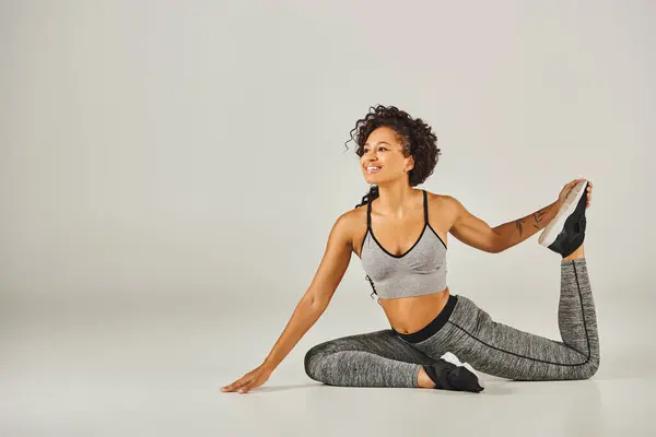 Junge Afroamerikanerin in aktiver Kleidung nimmt anmutig eine Yoga-Pose auf weißem Hintergrund ein. — Stockfoto
