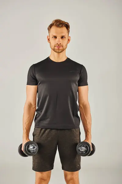 A young sportsman in active wear holding two dumbbells in front of a white background. — Stock Photo