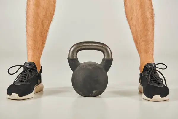 Young sportsman in active wear standing next to a kettlebell in a studio with a grey background. — Stock Photo
