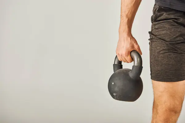 Um jovem desportista em uso ativo levanta vigorosamente um kettlebell em um estúdio com um fundo cinza. — Fotografia de Stock