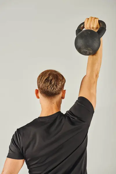 Un giovane sportivo in abbigliamento attivo solleva intensamente un kettlebell in uno studio con uno sfondo grigio. — Foto stock