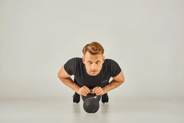 Ein junger Sportler in aktiver Kleidung hebt eine Kettlebell vor weißem Hintergrund in einem Fitnessstudio. — Stockfoto