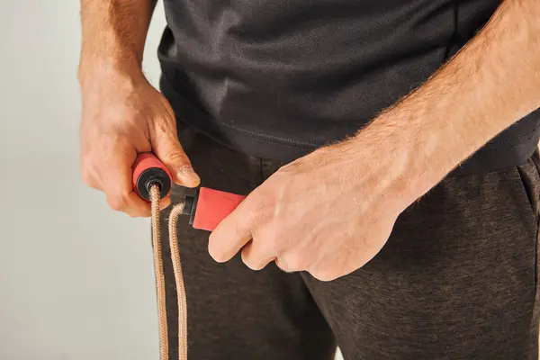 A young sportsman in active wear pulls a skipping rope with determination in a studio against a grey background. — Stock Photo