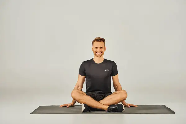 Um jovem desportista em desgaste ativo senta-se em uma pose de ioga em um fundo cinza, exalando calma e foco. — Fotografia de Stock