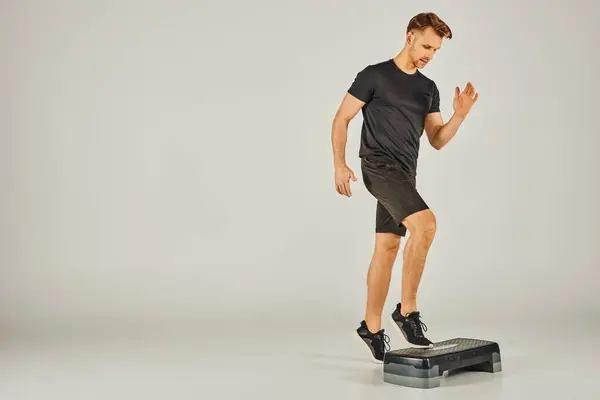 Un joven deportista en ropa activa utiliza un paso en un estudio sobre un fondo gris. - foto de stock